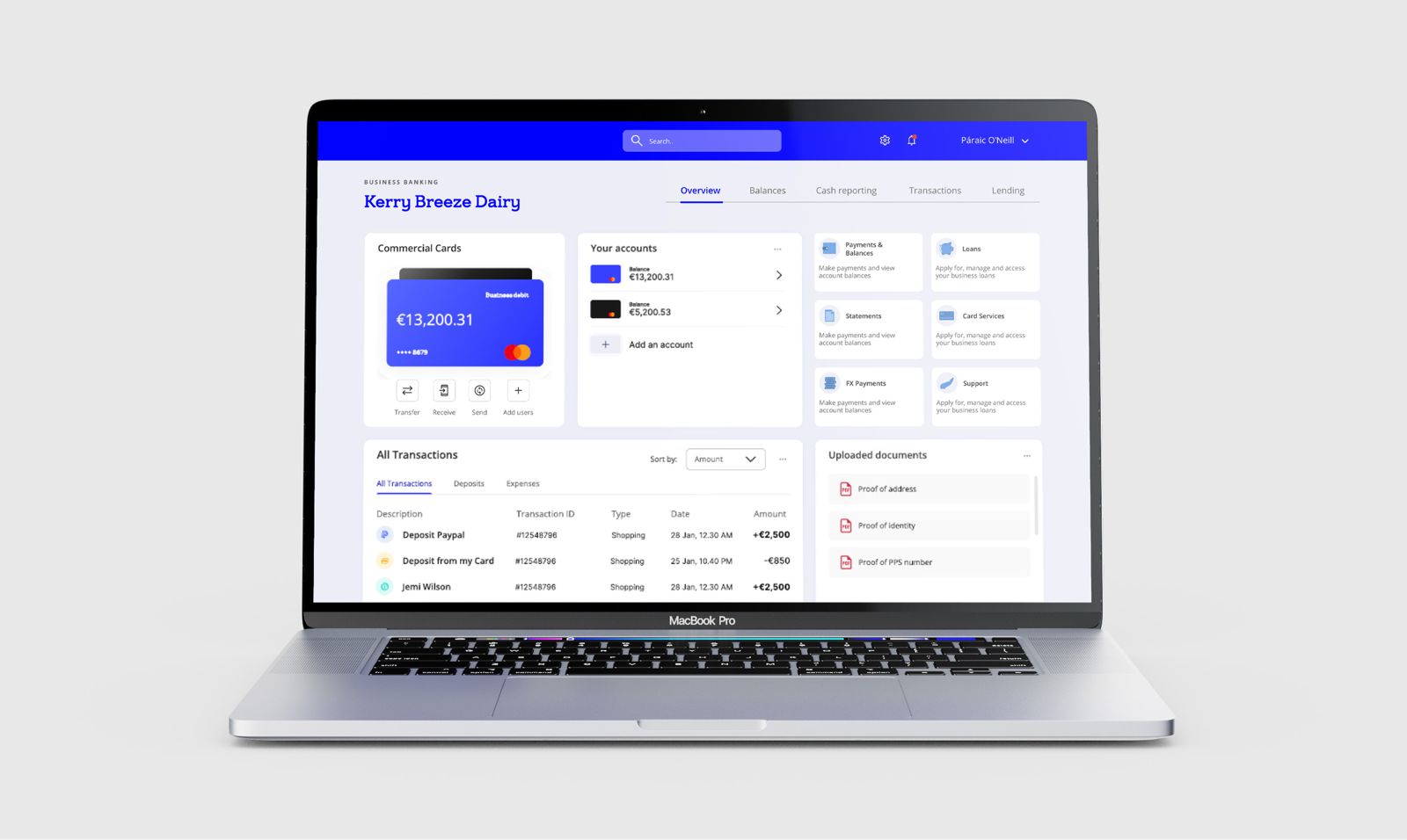 Laptop showing a business banking dashboard with commercial cards, account balances, quick actions, a transactions table and uploaded documents.